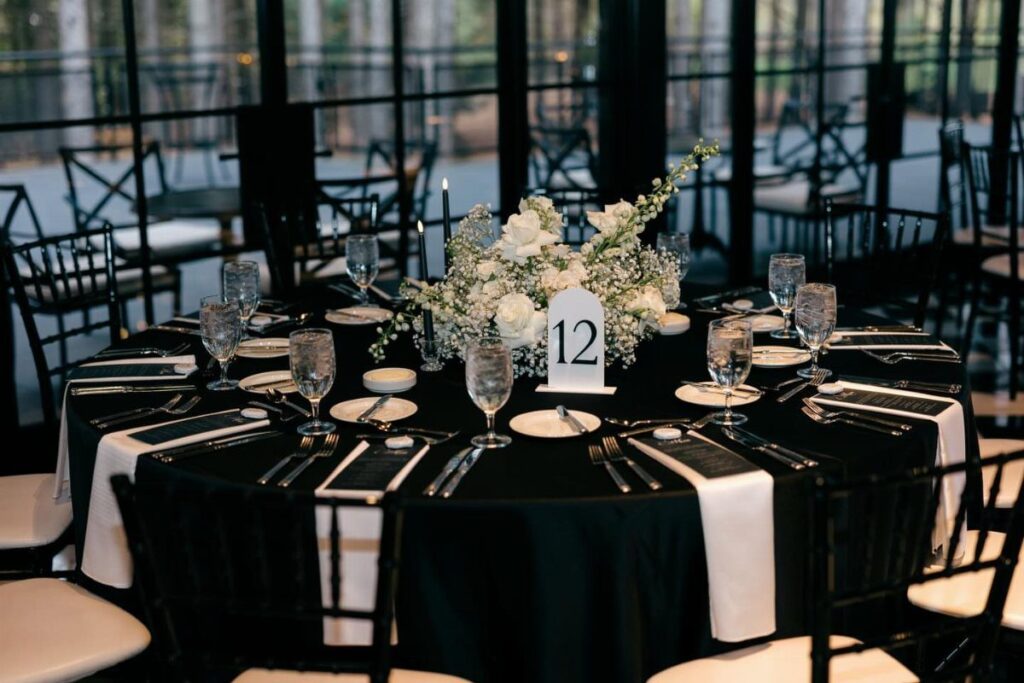 A round wedding table set with black linens, white flowers, and elegant glassware.