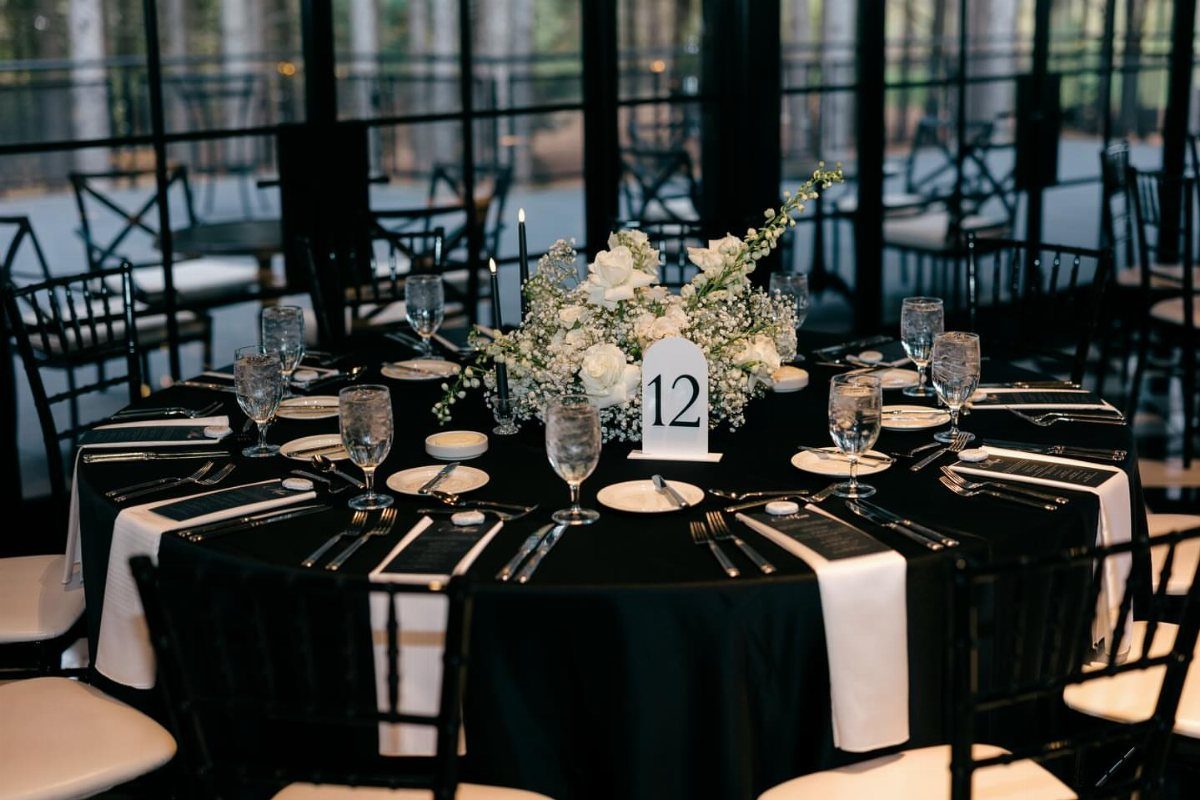 A round wedding table set with black linens, white flowers, and elegant glassware.