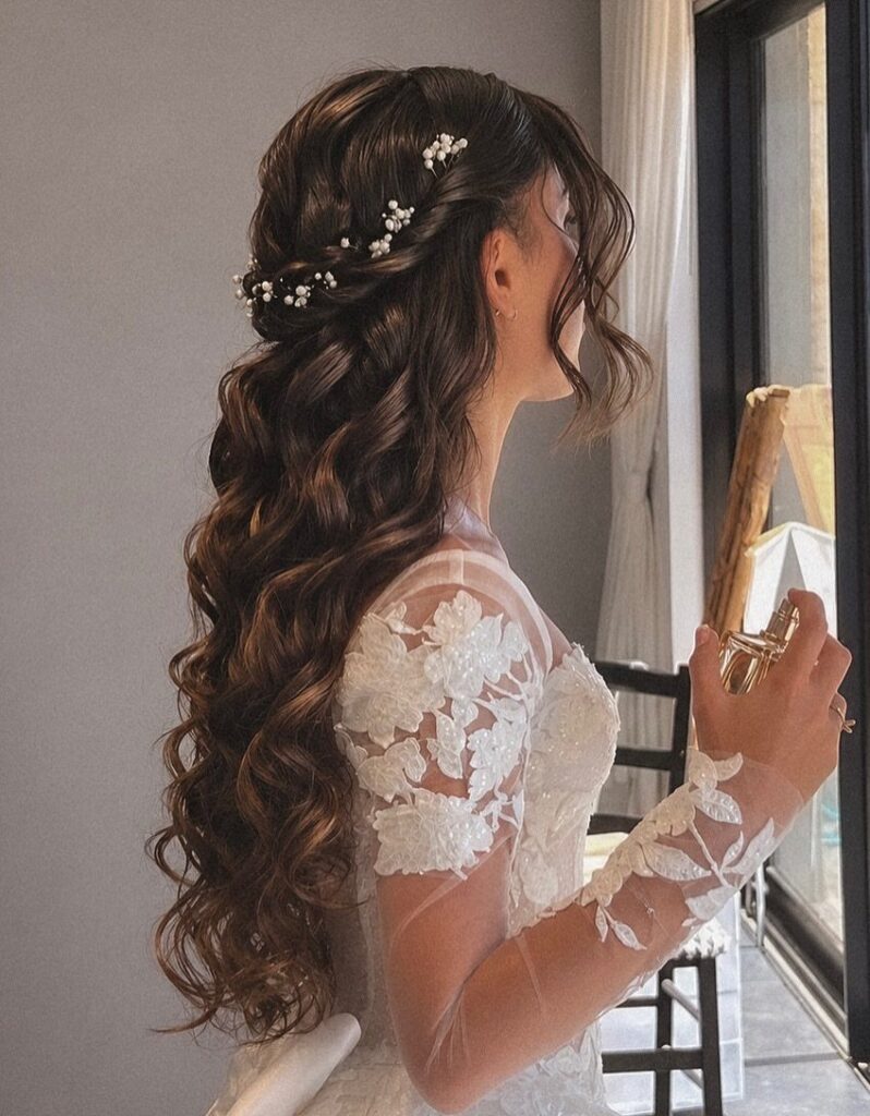 Woman with long wavy brunette hair styled with white floral hair accessories and lace wedding dress.