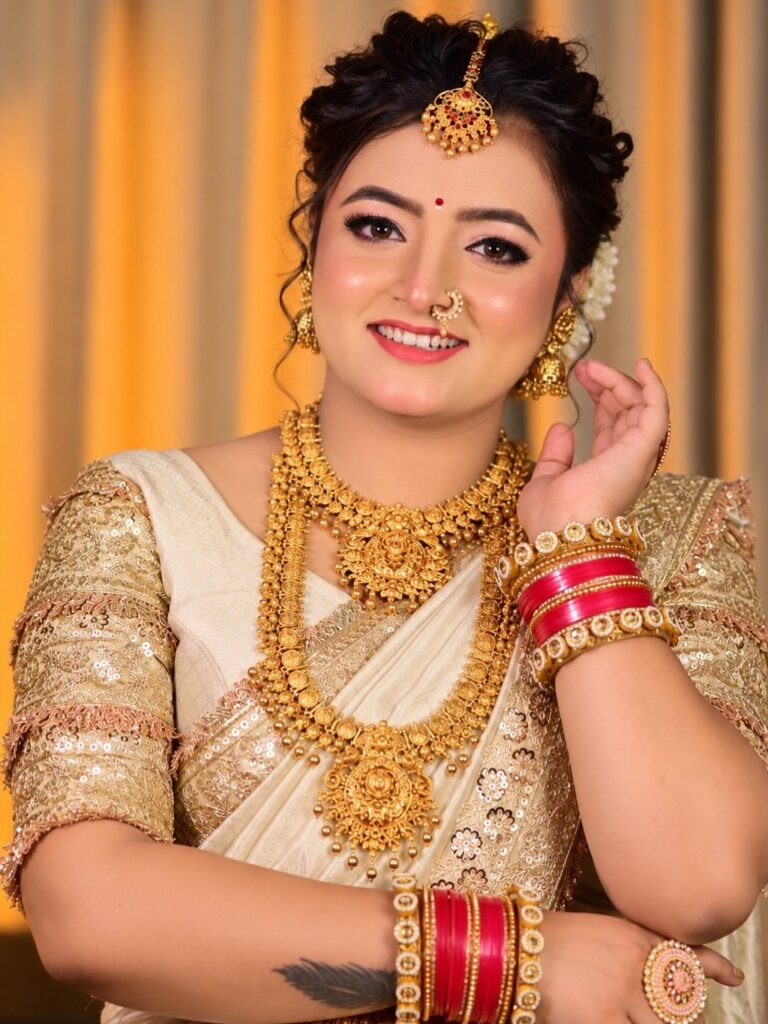 A smiling bride wearing traditional gold jewelry and a cream embroidered saree.