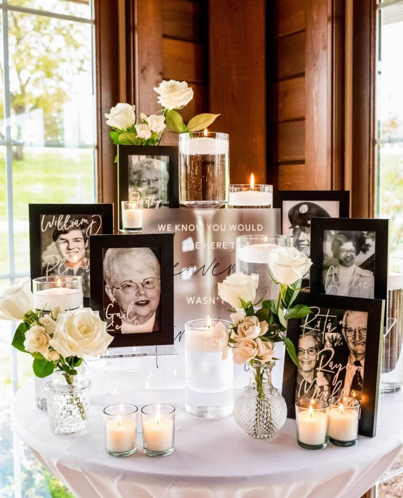 Framed black and white photographs, white roses, and lit candles arranged on a memorial table.