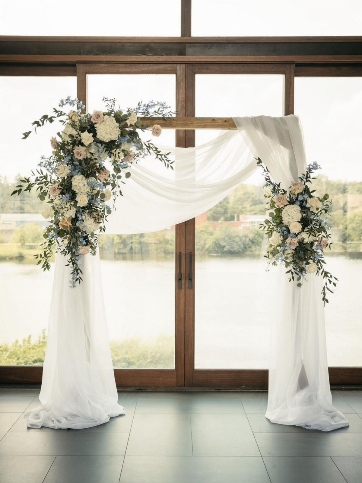 A wooden wedding arch decorated with white fabric and blue and white floral arrangements.