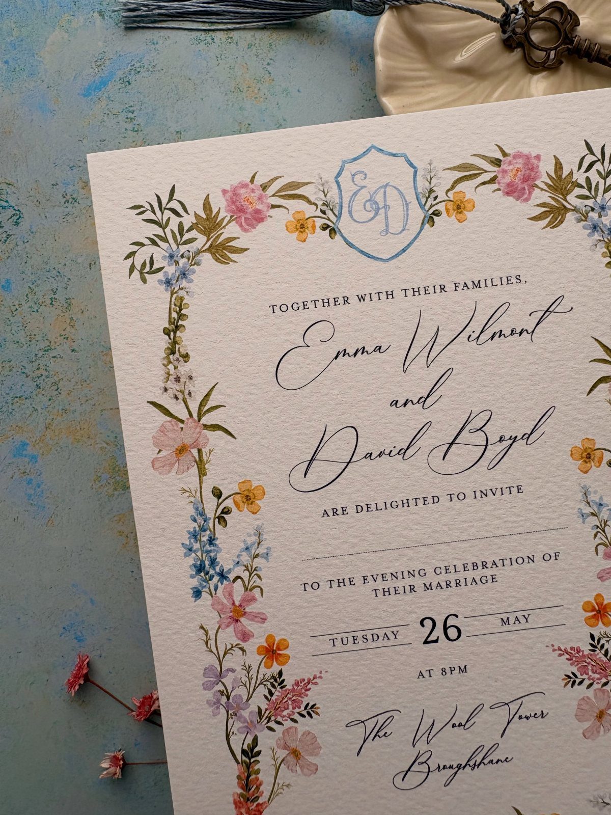 A floral wedding invitation with colorful wildflowers and elegant black calligraphy on textured paper.